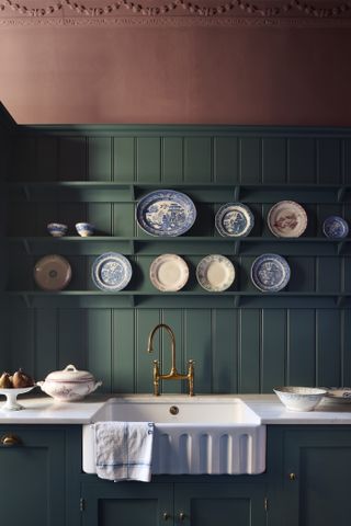 A traditional style pink and green kitchen sink area with open shelving and plates displayed