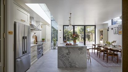 A large kitchen with an island and dining area next to the island. There is also a view of the double door fridge in the kitchen.