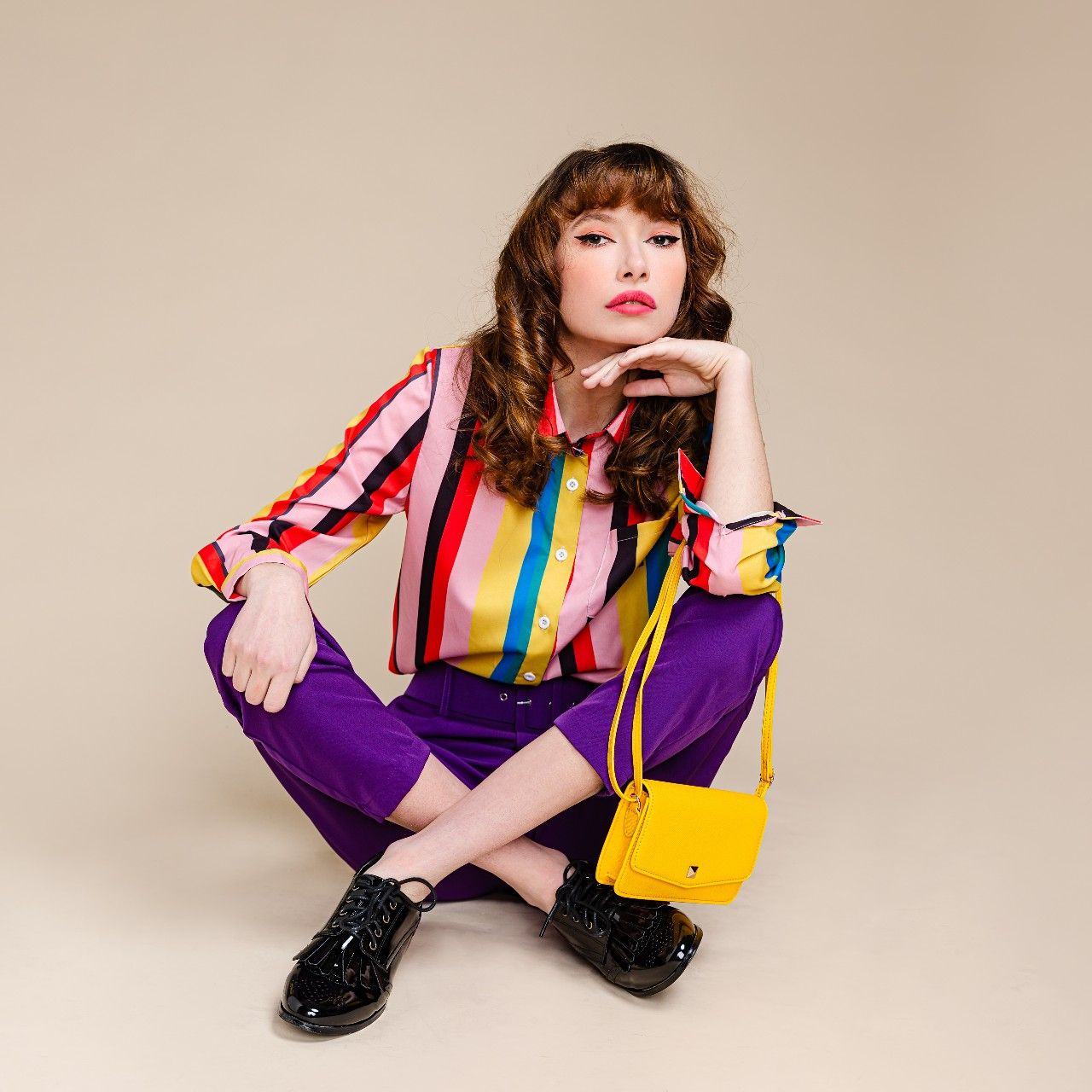 woman sitting wearing multi colored top and purple pants
