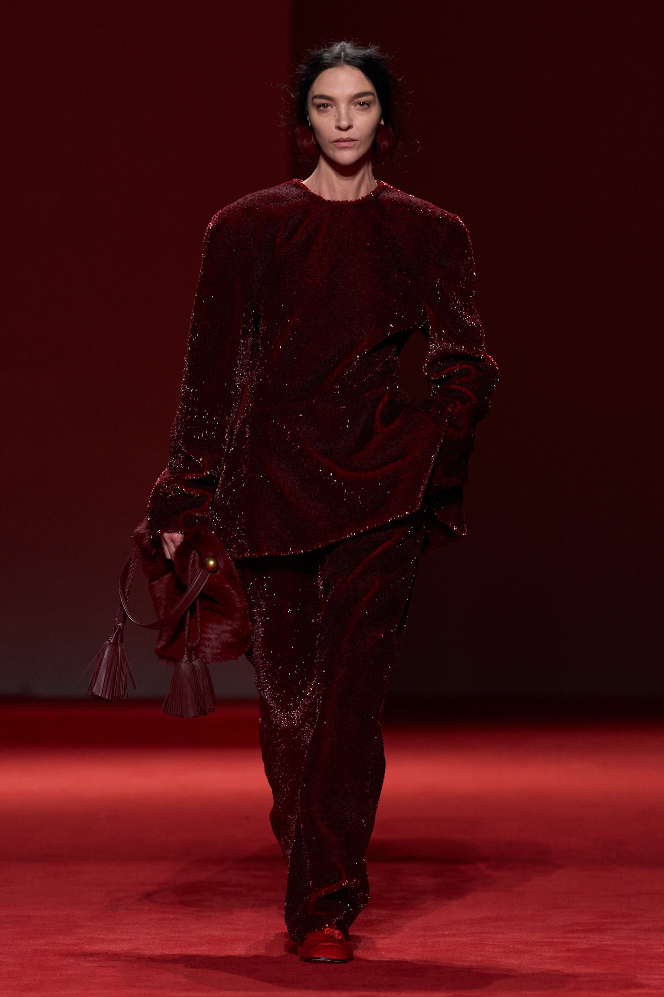 A model walking in the F/W 26 Bottega Veneta show during Milan Fashion Week wearing a red textured top and matching pants.