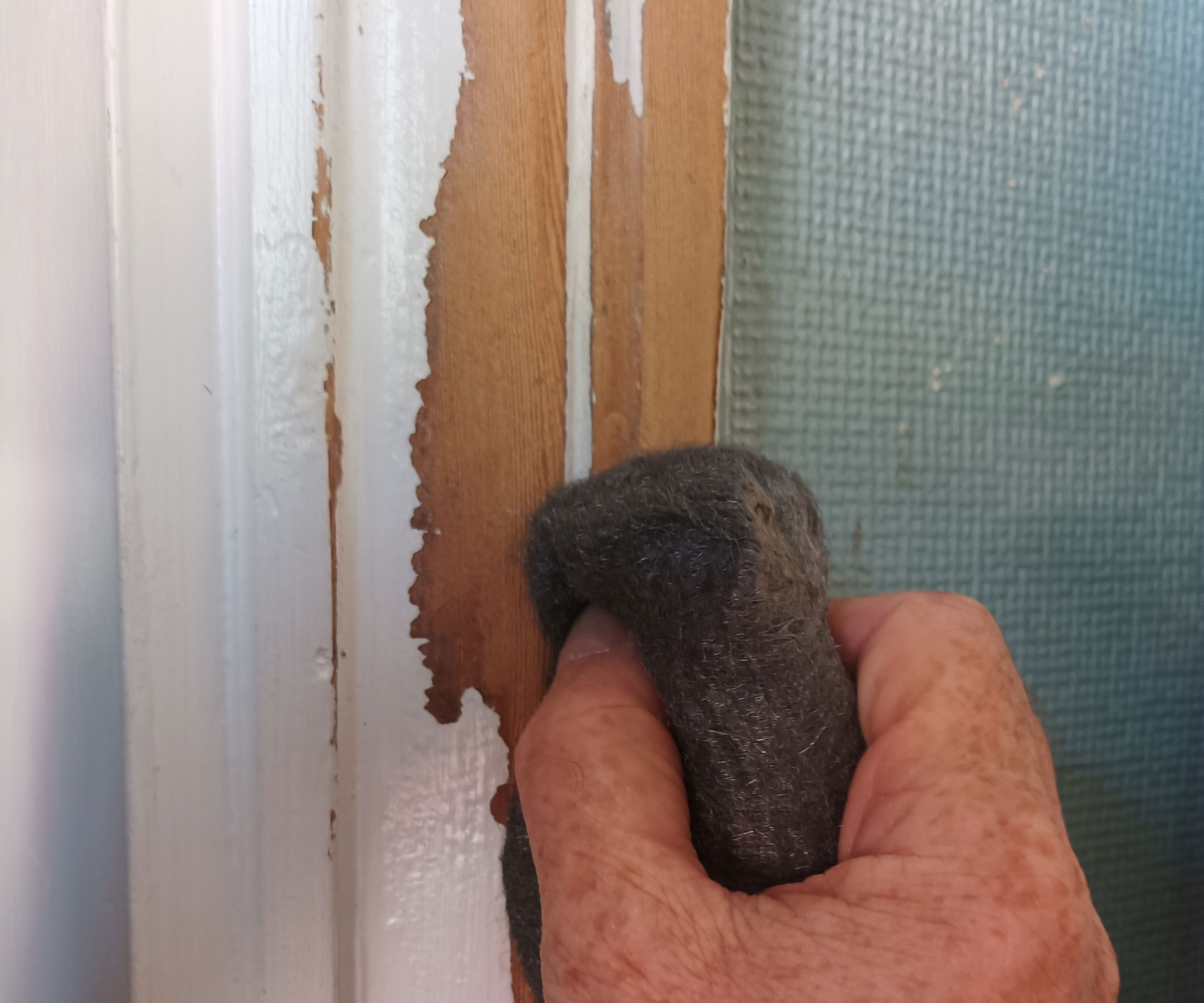 Hand holding wirewool removing paint from architrave