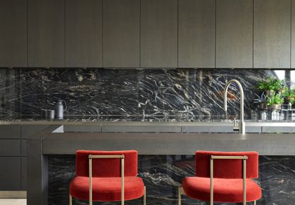 A kitchen with stone backsplash, and red counter stools