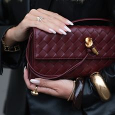 Hard BIAB Olga Liber with long, softly waved blonde hair worn in a center part, seen wearing a black satin lace camisole paired with loose charcoal silk trousers and an oversized black leather blazer. She completes the look with a gold-buckled YSL belt, oversized Prada shades, and a burgundy woven leather clutch