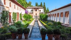 Image of the Alhambra Palace gardens in Spain, with rectangular water feature and fountains, surrounded by lush green planting