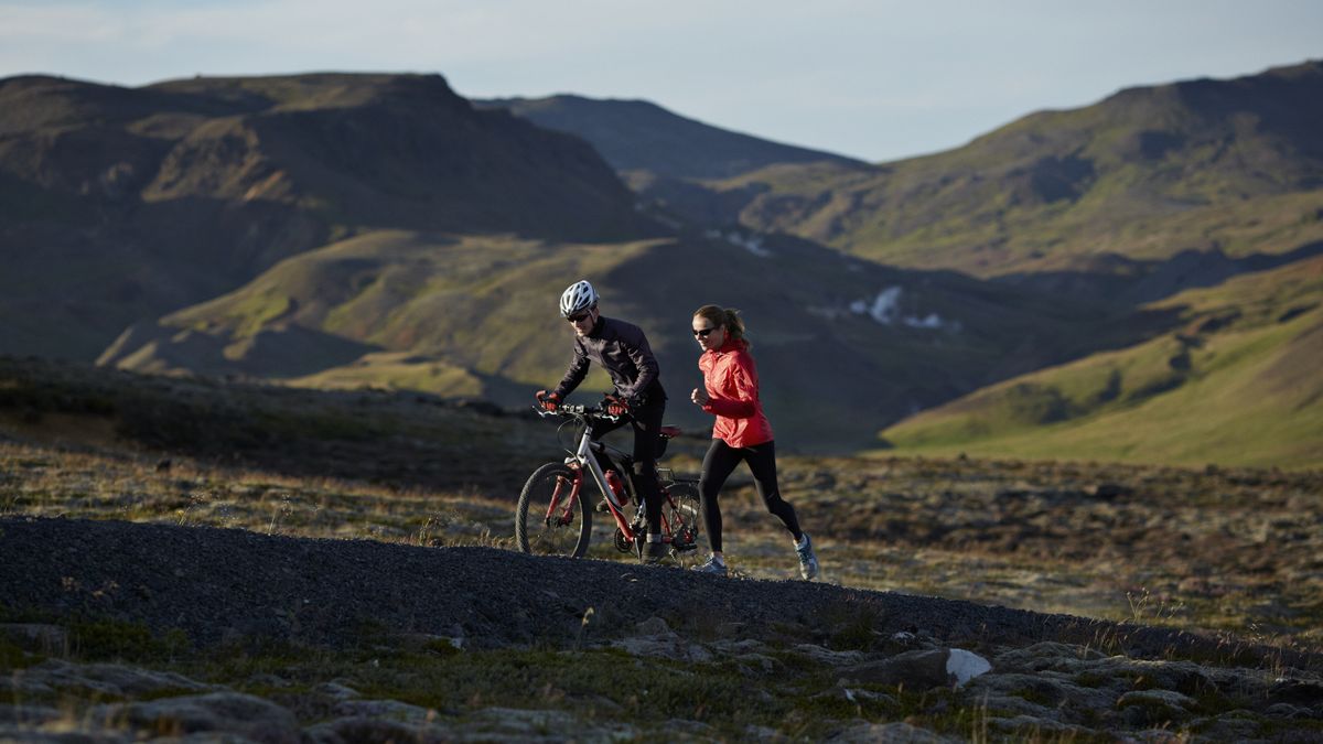 Couple running &amp; biking together on mountain trail