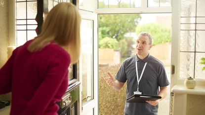A door-to-door salesman stands on the front porch while talking to a female homeowner.