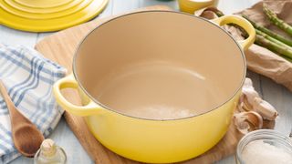 A yellow casserole dish on a kitchen worktop, with asparagus, garlic, salt and a wooden spoon nearby