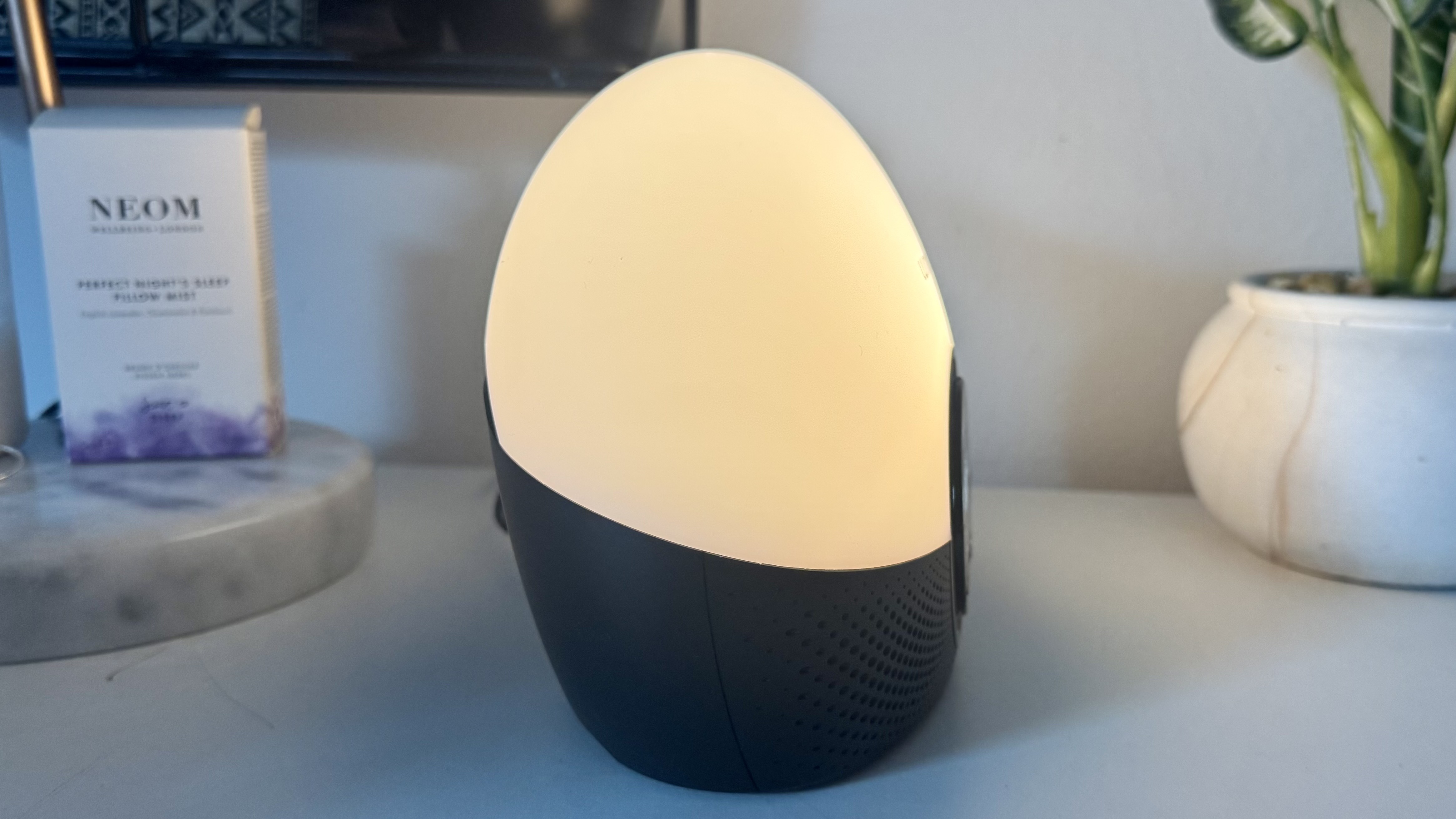Lumie Bodyclock Glow 150 sunrise alarm clock on bedside table with NEOM pillow spray and plant