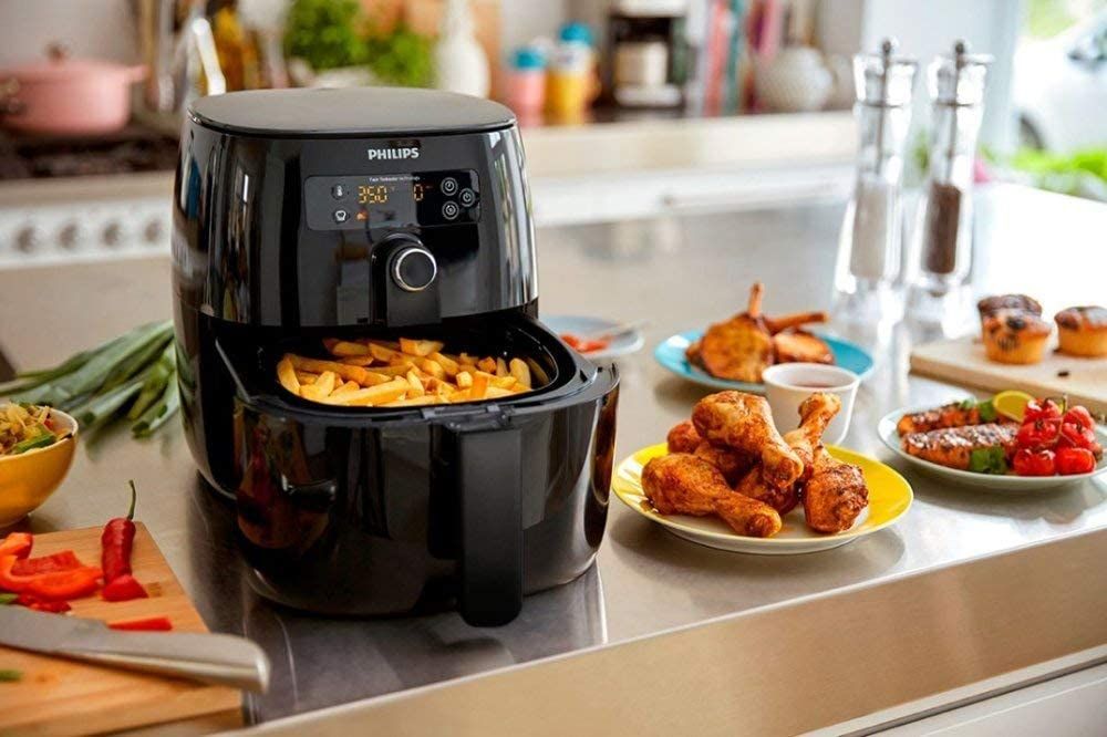 A black Philips air dryer with cooked chicken drumstick pieces on plate in kitchen