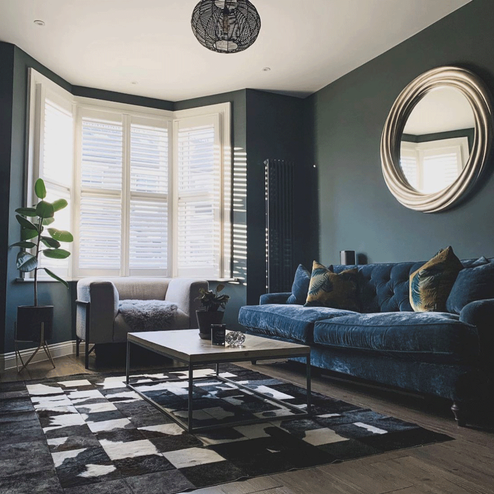 Charcoal blue living room with blue sofa and mustard cushions and round gold mirror