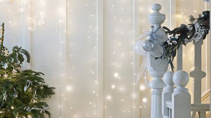 Curtain string lights along way leading up staircase beside Christmas tree