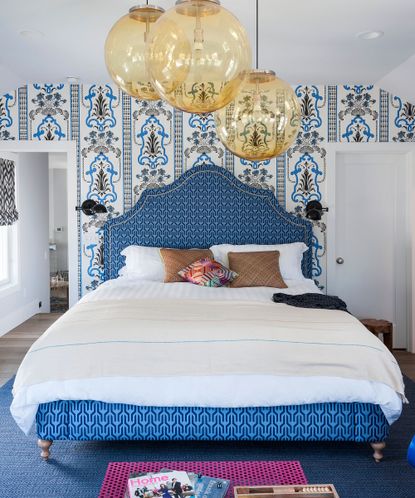 Blue bedroom ideas with blue patterned wallpaper and headboard, large round glass ceiling lights and white bedlinen.