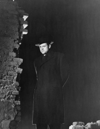 orson welles wears a trench coat and hatand stands by a crumbling brick building in a promotional shot for The Third Man