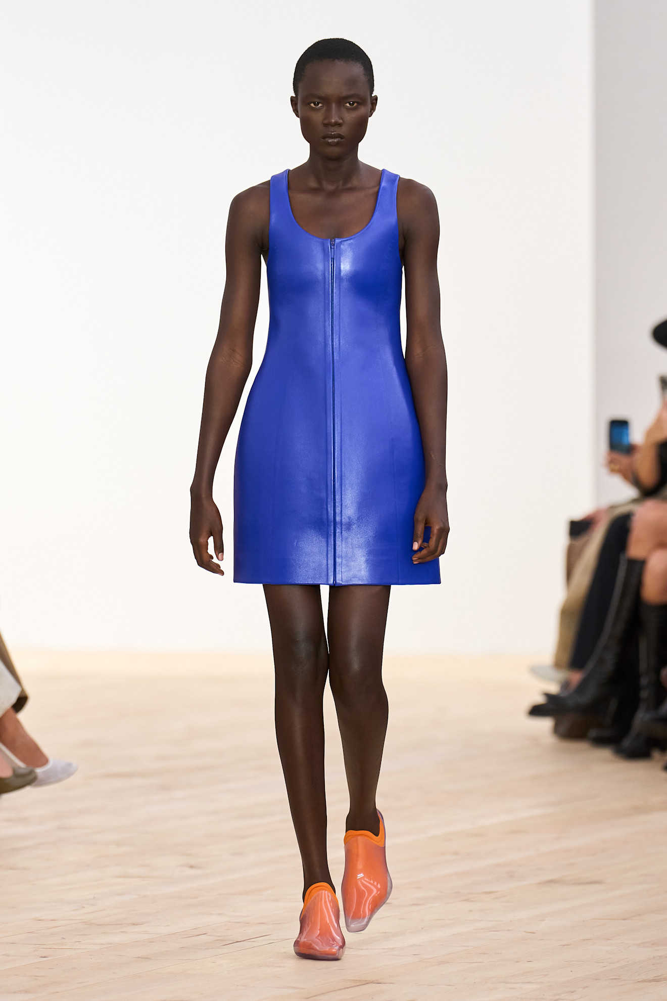 A Loewe model wearing a bright blue scoop neck leather shift dress styled with PVC pointed loafers and bright orange socks.