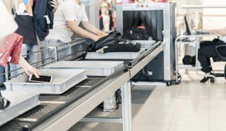 Travellers loading items into airport security trays ahead of x-ray machine