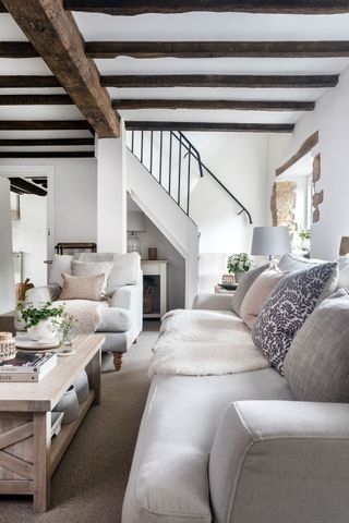living room with beams and exposed stone walls with staircase behind and white sofas with coffee table