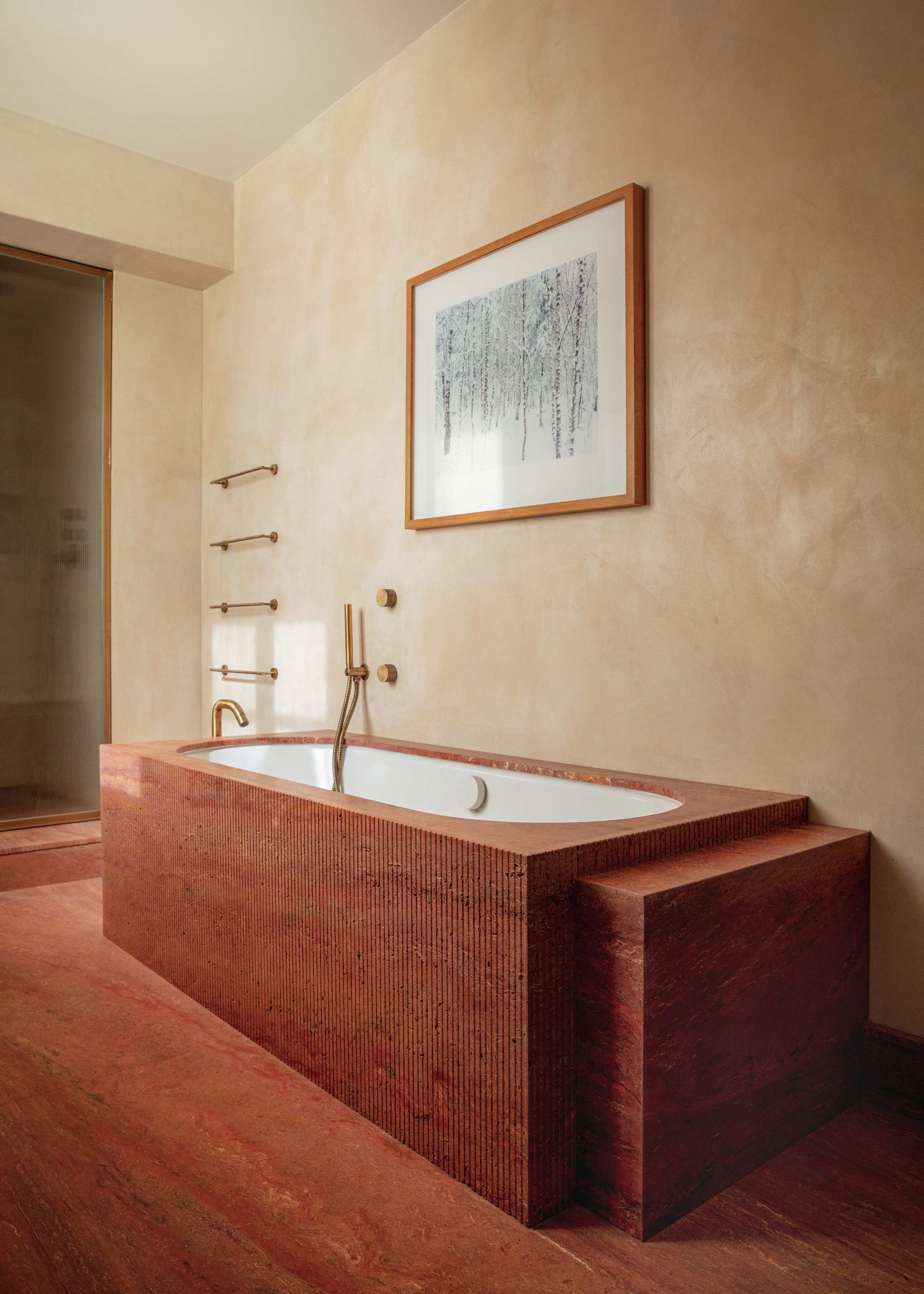 Bathroom with beige plaster walls, red marble floor and fluted red marble bath