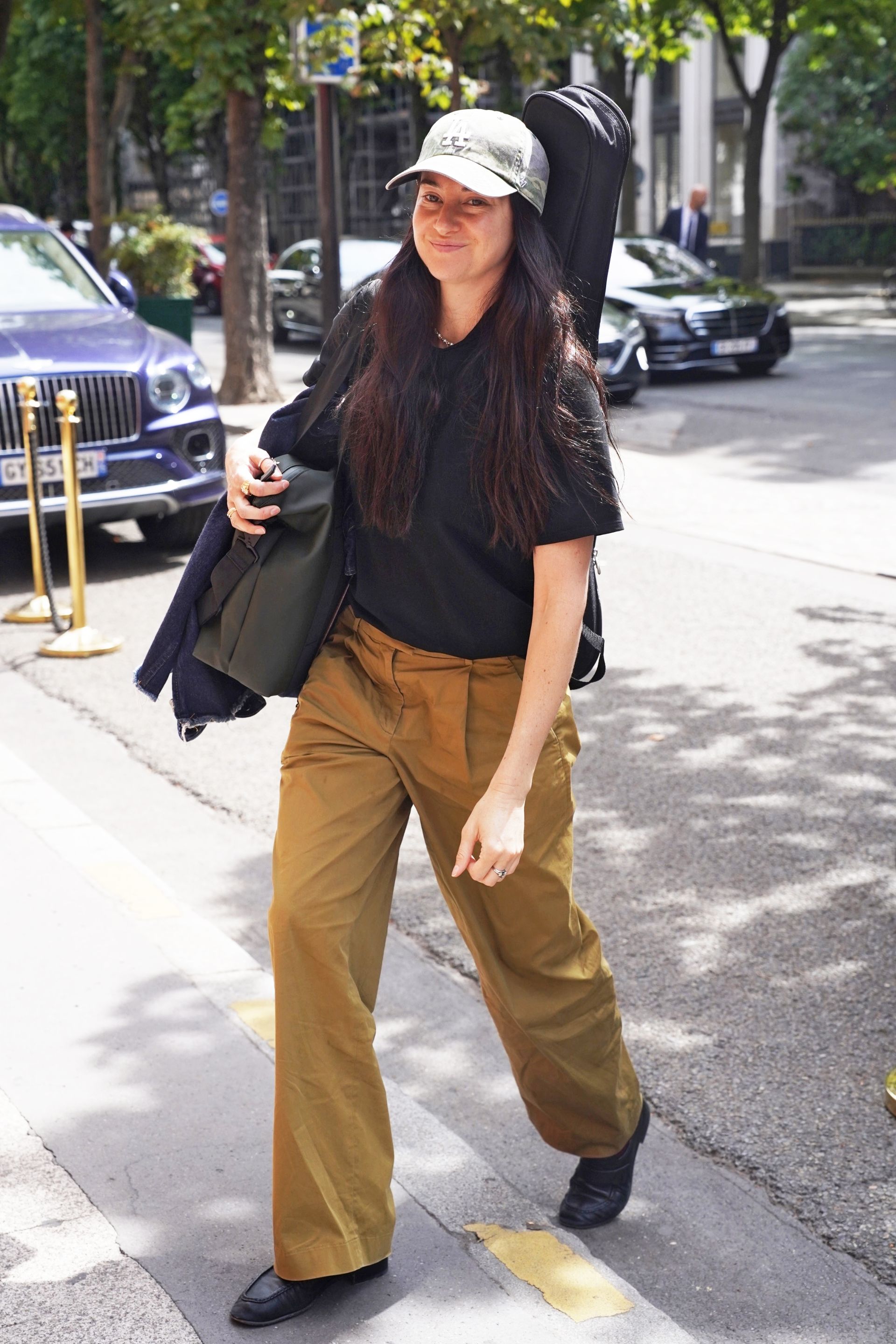 Shailene Woodley wearing a green baseball cap, black t-shirt, olive pants, and black loafers