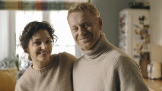 Greta and Jacek wearing cream jumpers and looking happy, smiling into the camera in Just One Look