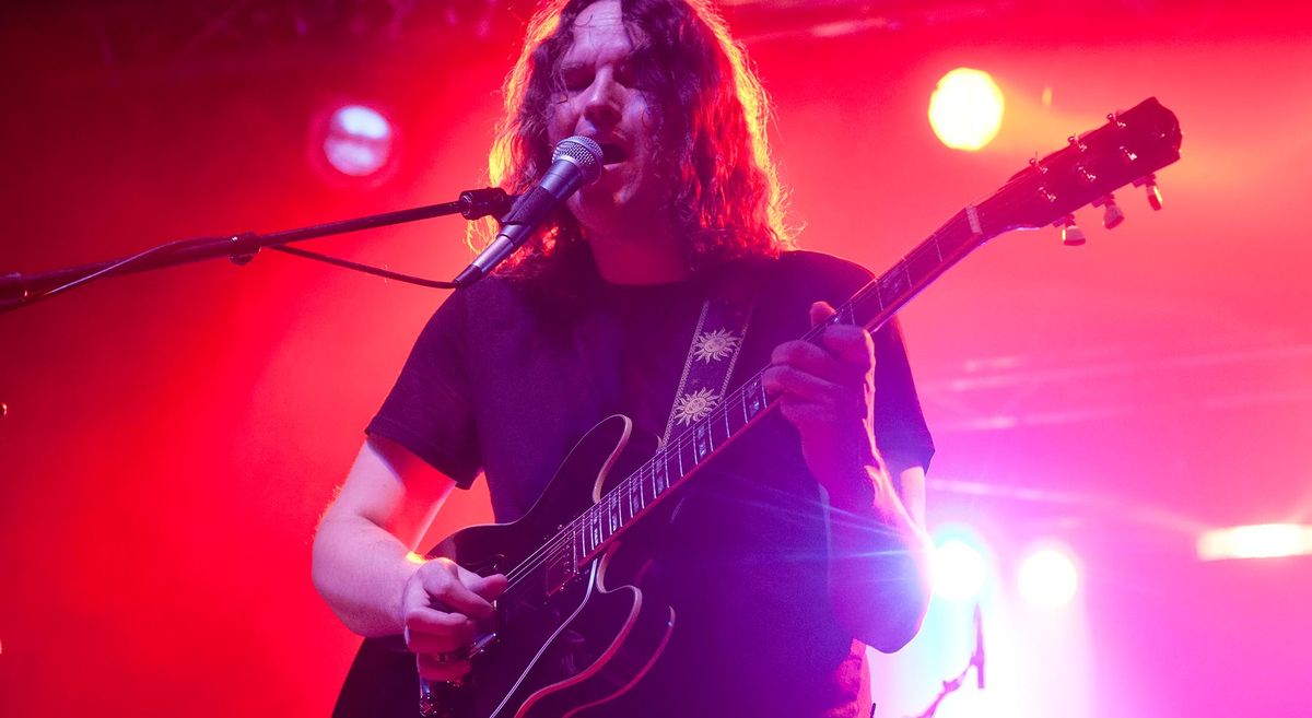 Torsten Kinsella plays a Gibson semi-hollow on a stage lit up in red, pink and orange.