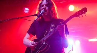 Torsten Kinsella plays a Gibson semi-hollow on a stage lit up in red, pink and orange.