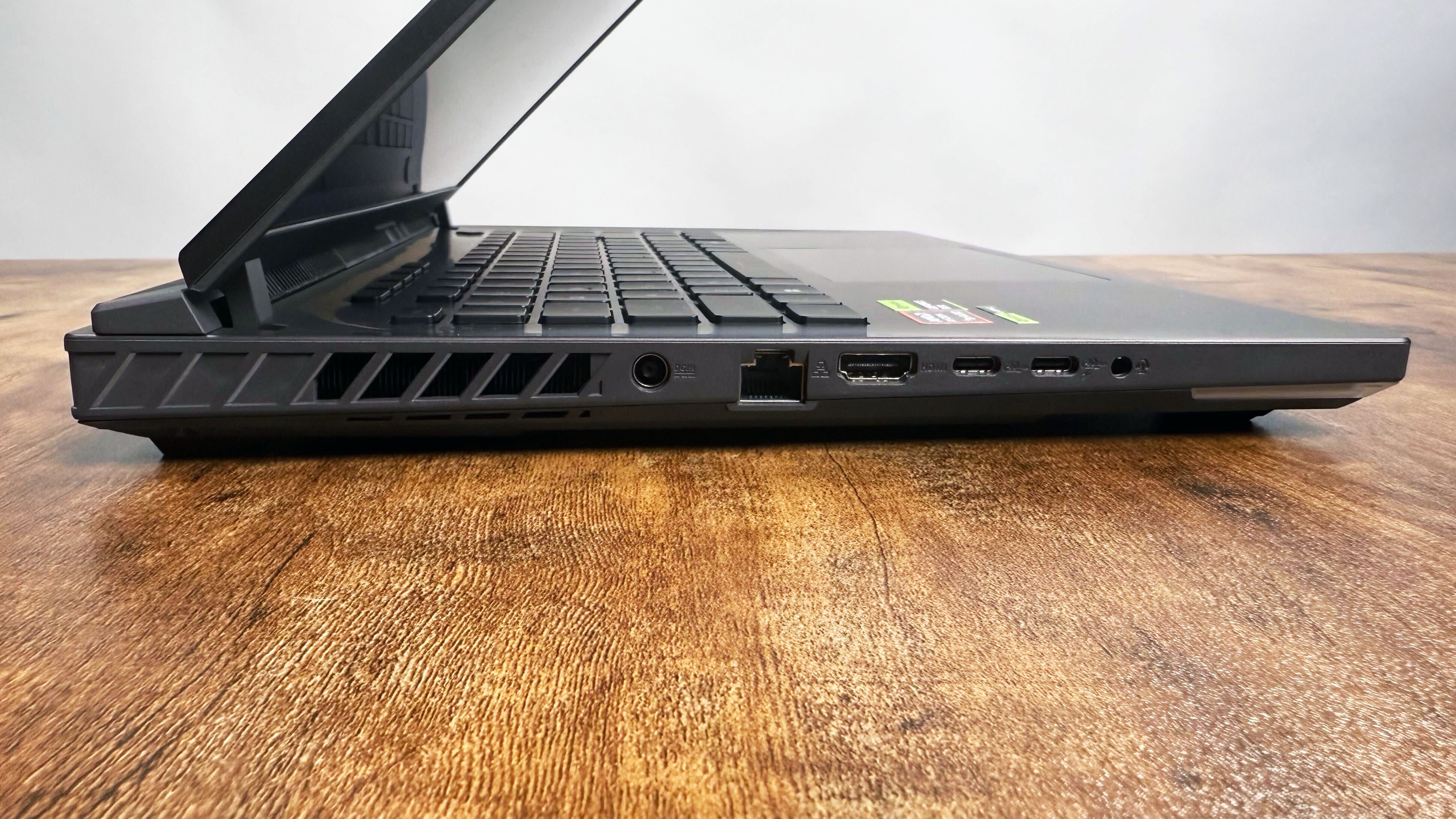 Close up of the left-side ports on the Asus ROG Strix G16 (G614FR) gaming laptop on a wooden desk against a gray background.