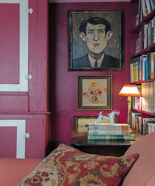 pink living room with painted pink walls and cushions, books and paintings on walls