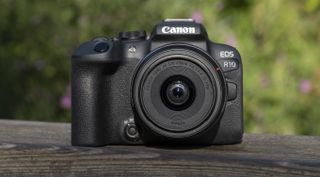 Et reisekamera av typen Canon EOS R10 plassert på et rekkverk av tre.