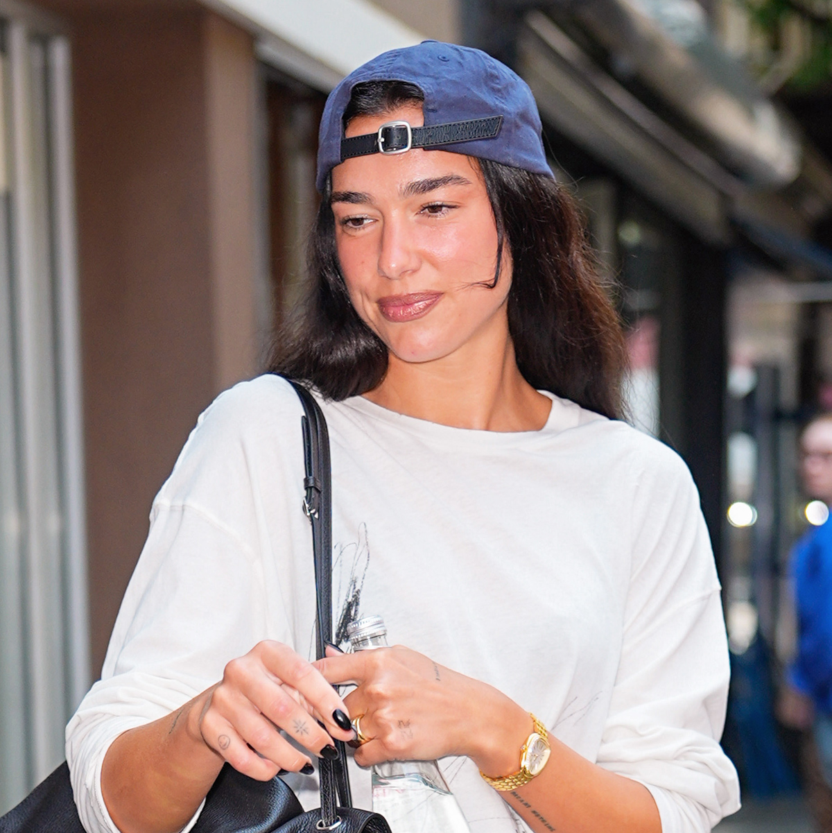 Dua Lipa exiting Electric Lady in NYC wearing a backwards baseball cap, white long-sleeve T-shirt, cut-off denim shorts, and a black Chanel Maxi Flap bag and burgundy Chanel Coco Beach ballet flats 
