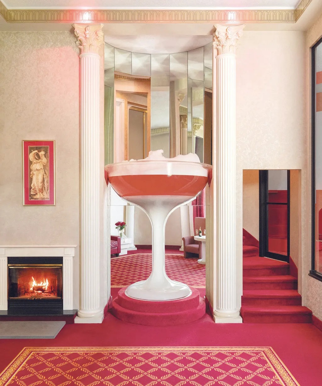 A 7-foot-tall champagne glass serves as a colossal bathtub in a velvety pink and white, pillared hotel room.