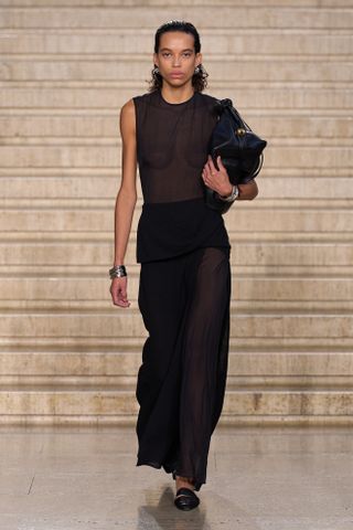 A model wearing a black sheer high-neck maxi dress at the S/S 25 Tove show showcasing the modern socialite trend.