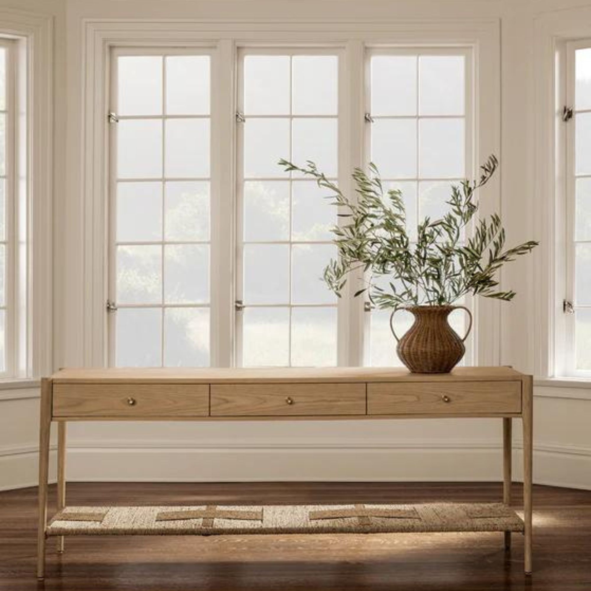 A light wooden console table in front of a large picture window