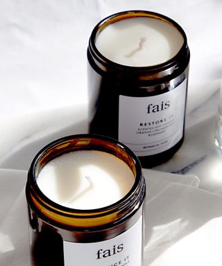 Two white candles in amber glass jars. Unburned, white braided wicks. on white marble surface