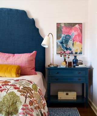 bedroom with navy headboard, navy blue nightstand, pink artwork and pillows