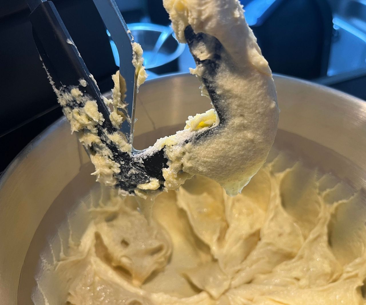 A close up of a black silicone mixer attachment with flour stuck to it, above a bowl of cake batter
