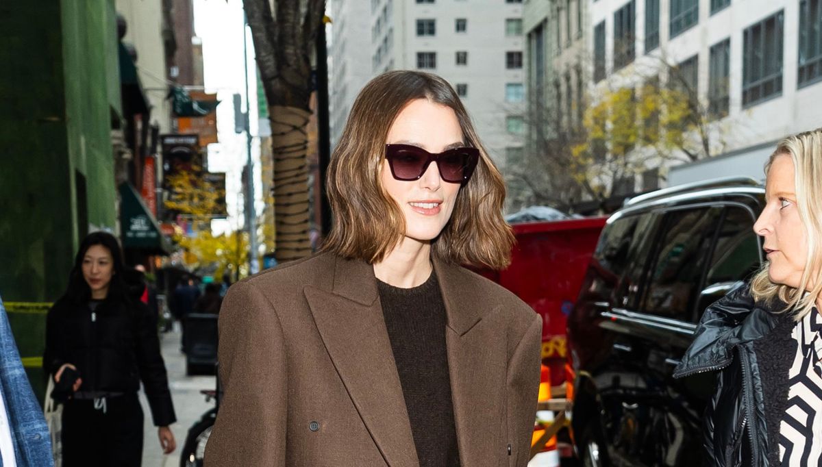 Keira Knightley porte le meilleur blazer marron chocolat avec une jupe rose blush, un pull couleur café et des talons blancs à bride arrière.