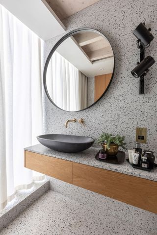 a round mirror in a modern contemporary bathroom with floating cabinets and oval washbasin