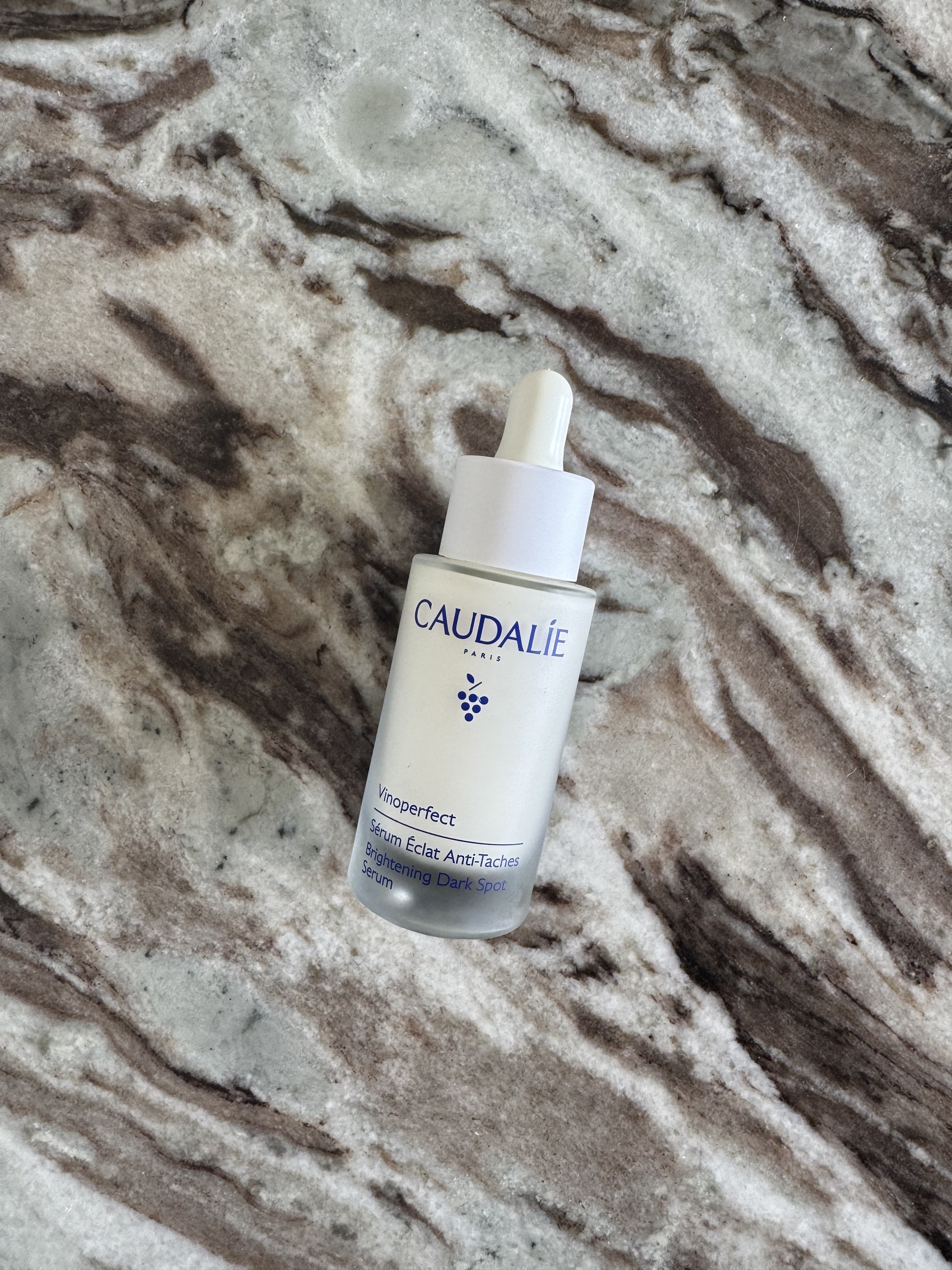A bottle of Caudalie Vinoperfect serum on a marble background