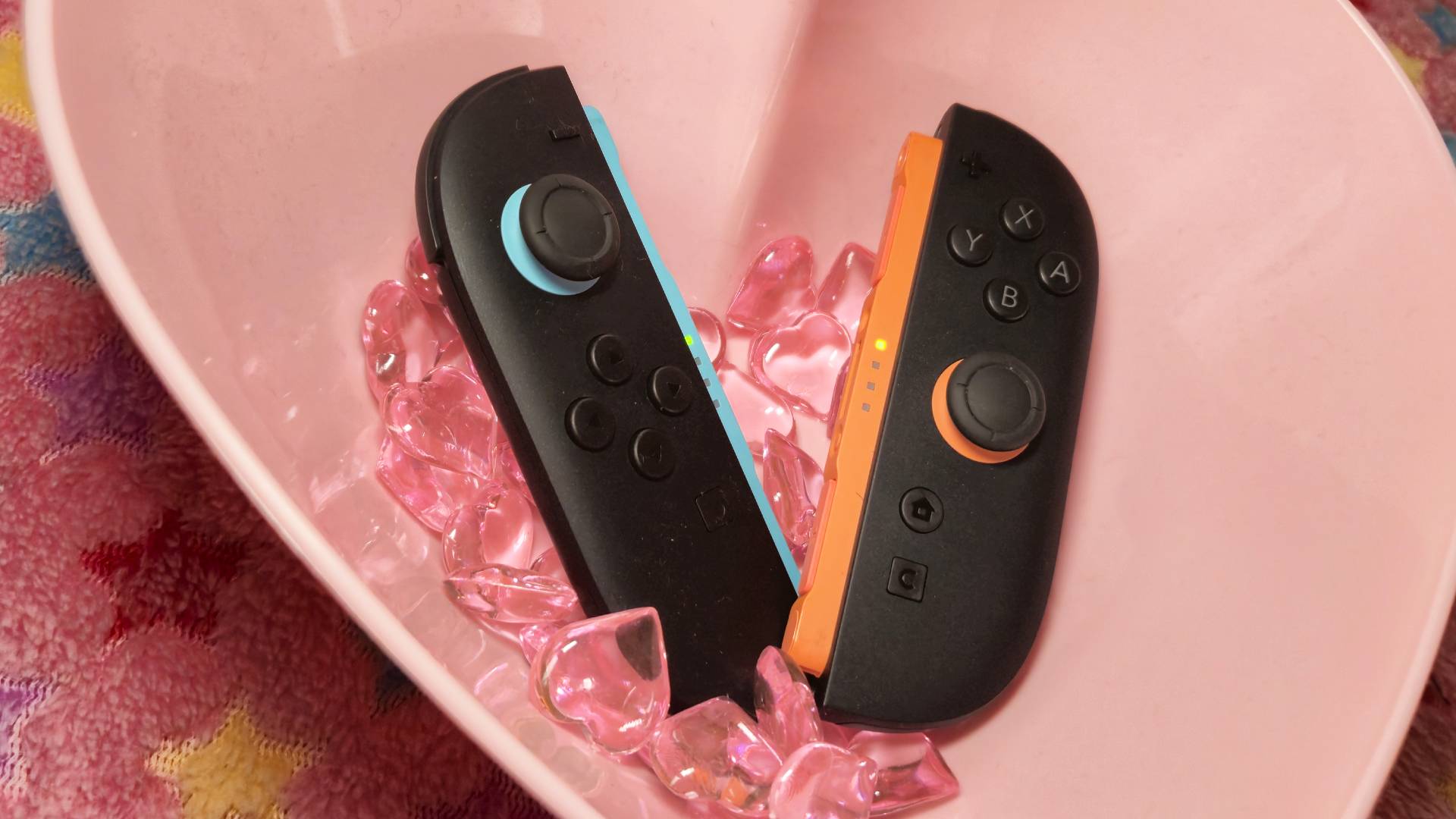 Image of the Switch 2 Joy-Con controllers sitting a love heart-shaped bowl with pink, plastic hearts around them.