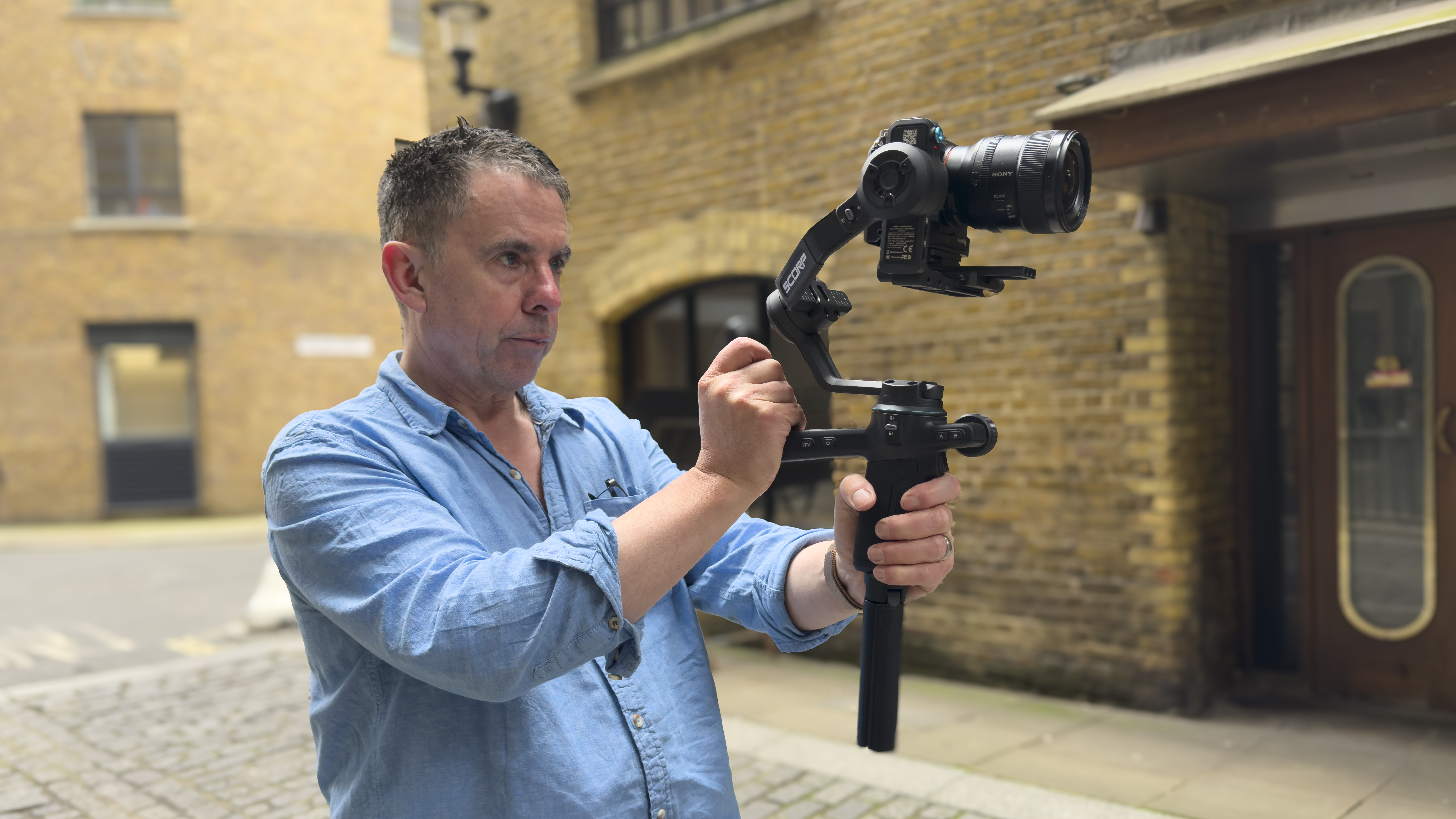 Man holding a camera mounted on a handheld gimbal in a cobbled street
