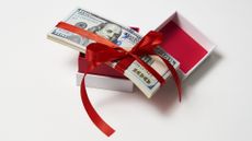 Hundred-dollar bills inside a gift box with a red ribbon.