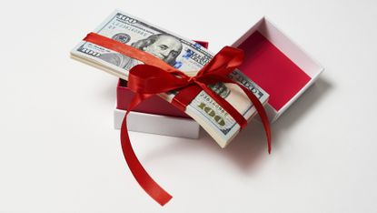 Hundred-dollar bills inside a gift box with a red ribbon.
