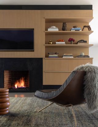 A living room with a comfy chair and a fur throw facing a fireplace and tv