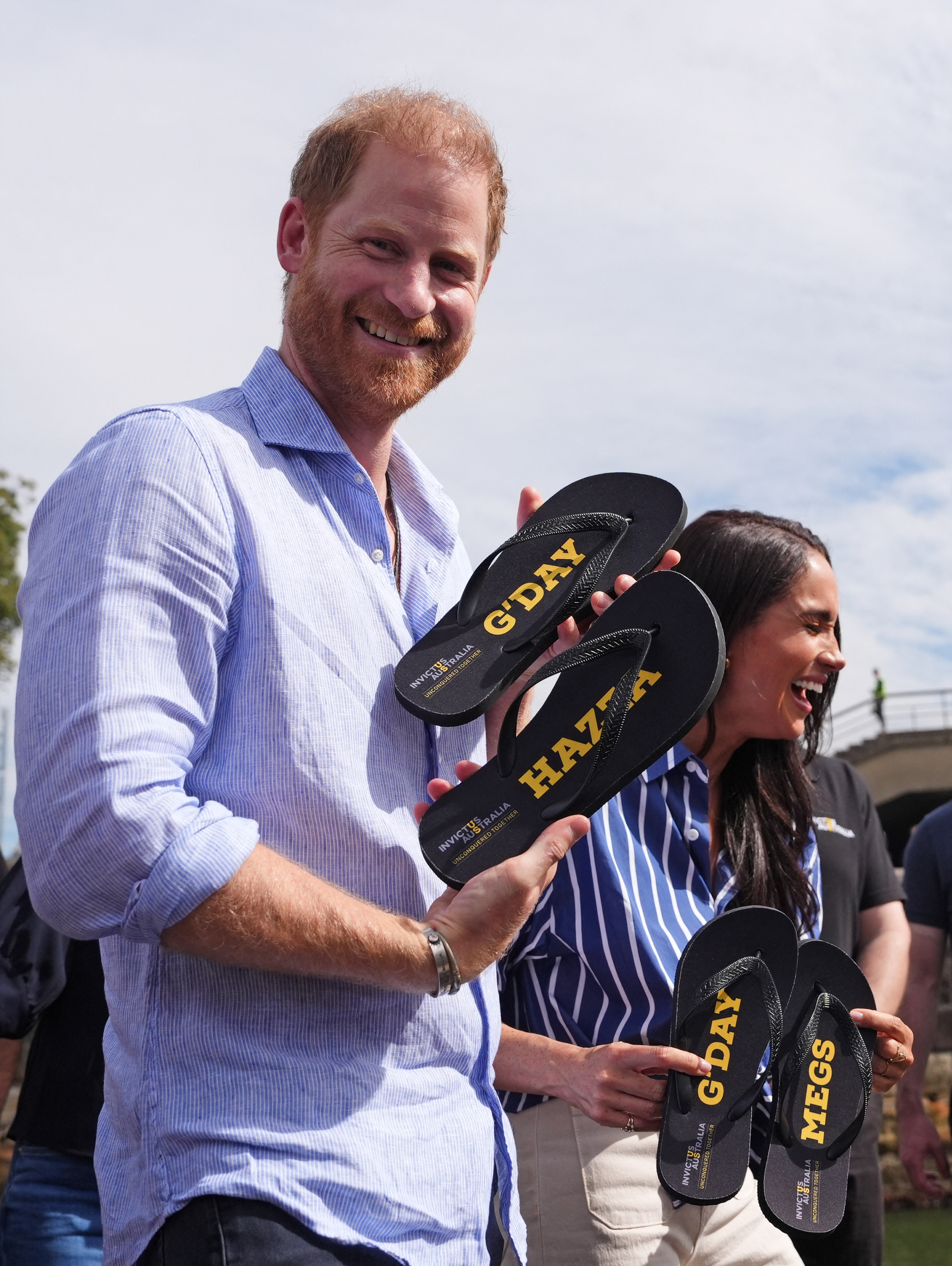 Prince Harry and Meghan Markle laughing and holding flip-flops