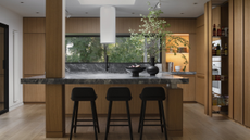 a wood kitchen with a stone topped kitchen island with a column running through