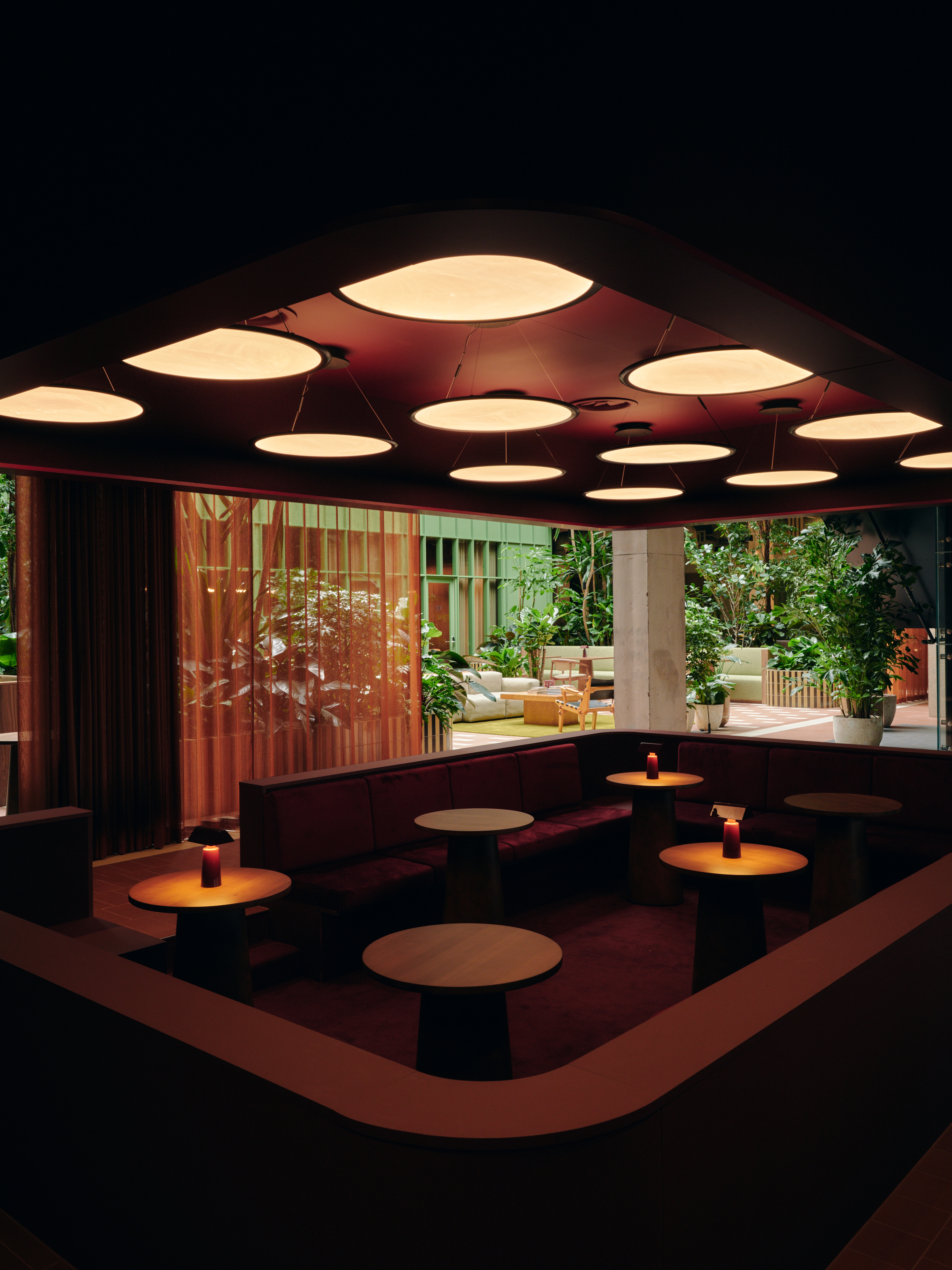 A series of interior shots of a workspace designed with terracotta-hued checkered floors, coffered ceilings in wood and back-lit blocks, pendant, see-through lighting, mid-century furniture,