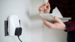 Cable plugged into a smart plug in the wall. A person is holding a phone in their hand in the background