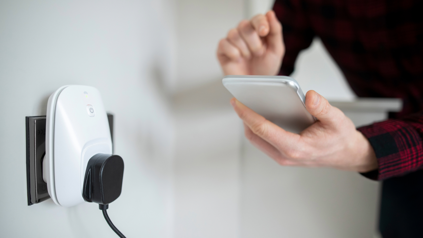 Cable plugged into a smart plug in the wall. A person is holding a phone in their hand in the background