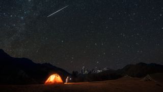 a meteor shower in the sky above a tent