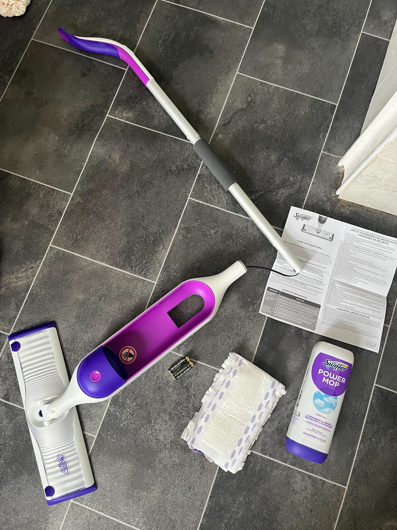 a purple and white Swiffer power mop in sections on a black bathroom floor